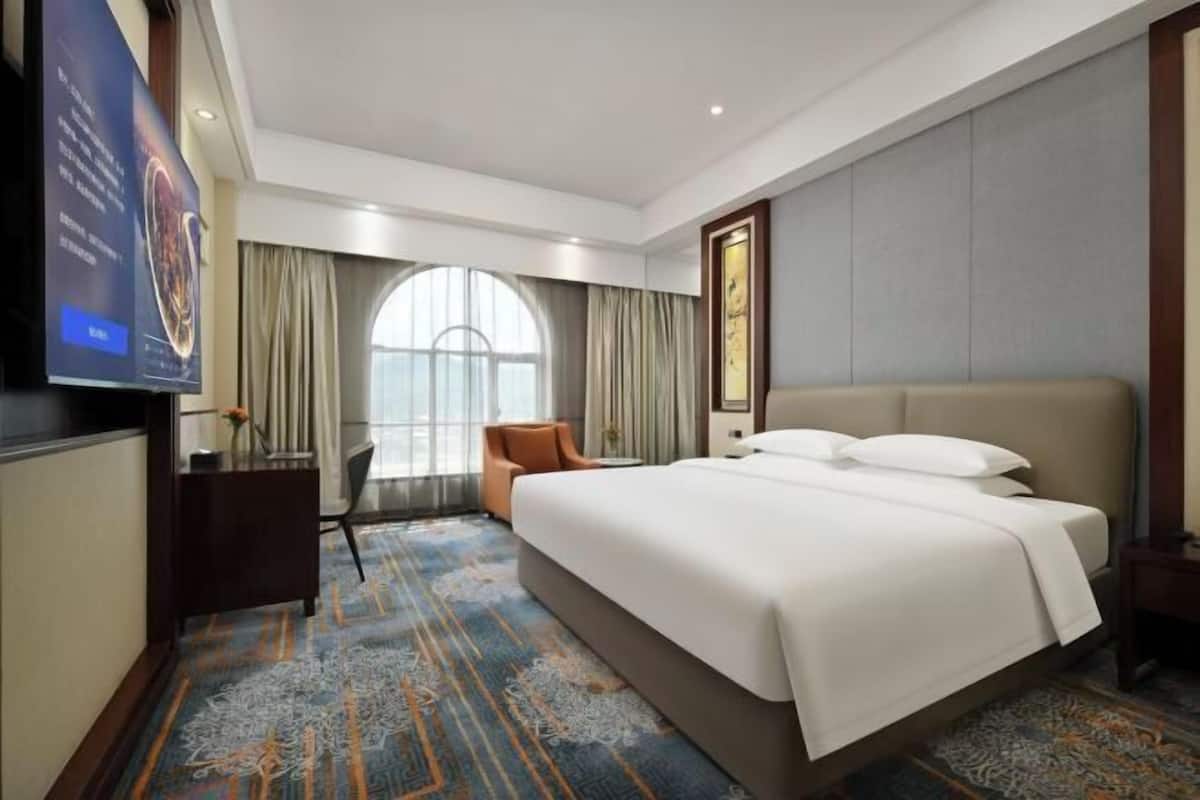 A hotel room with a large bed, a desk, a chair, and a television.