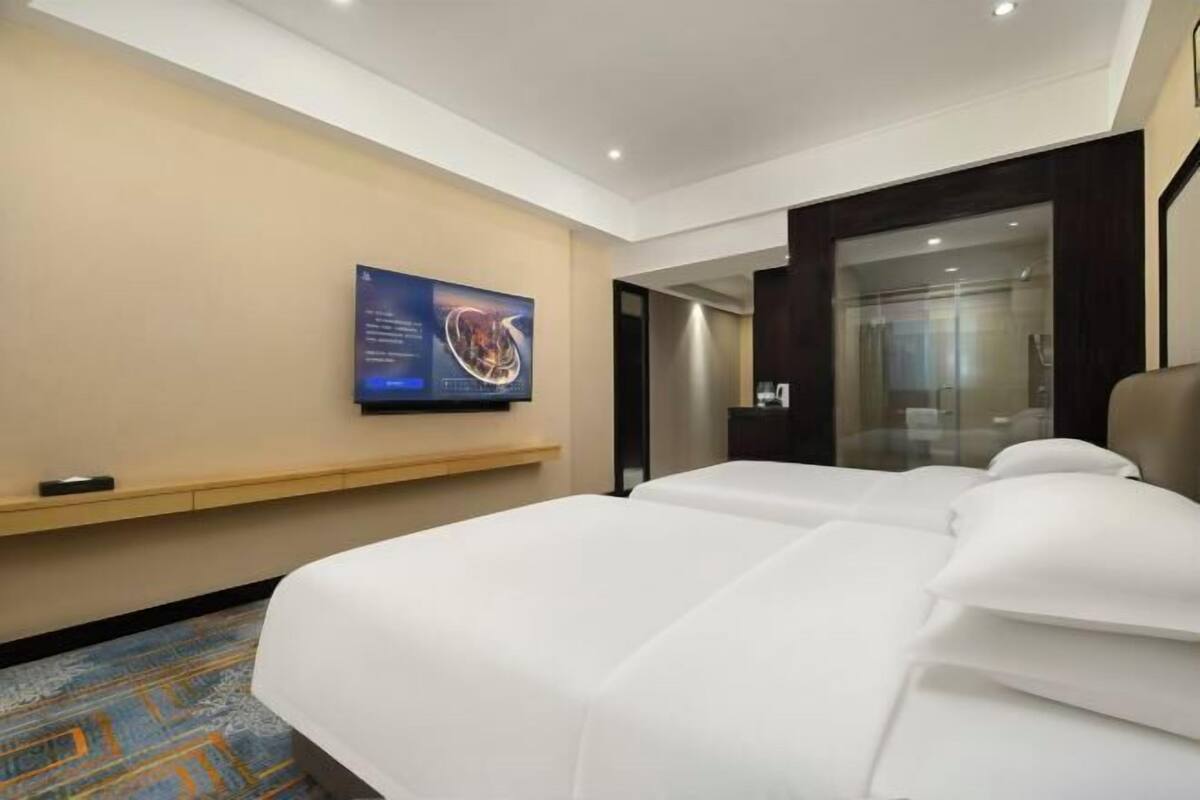 A hotel room with a large bed, a flat-screen TV mounted on the wall, and a carpeted floor.