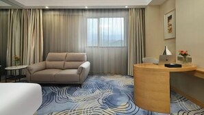 A hotel room with a sofa, a desk with a laptop, a small table with a vase, and a large window with curtains. - Dongguan Xiegang FONTOO Hotel (Dongguan)