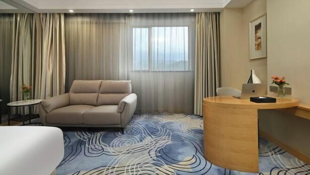 A hotel room with a sofa, a desk with a laptop, a small table with a vase, and a large window with curtains. - Dongguan Xiegang FONTOO Hotel (Dongguan)