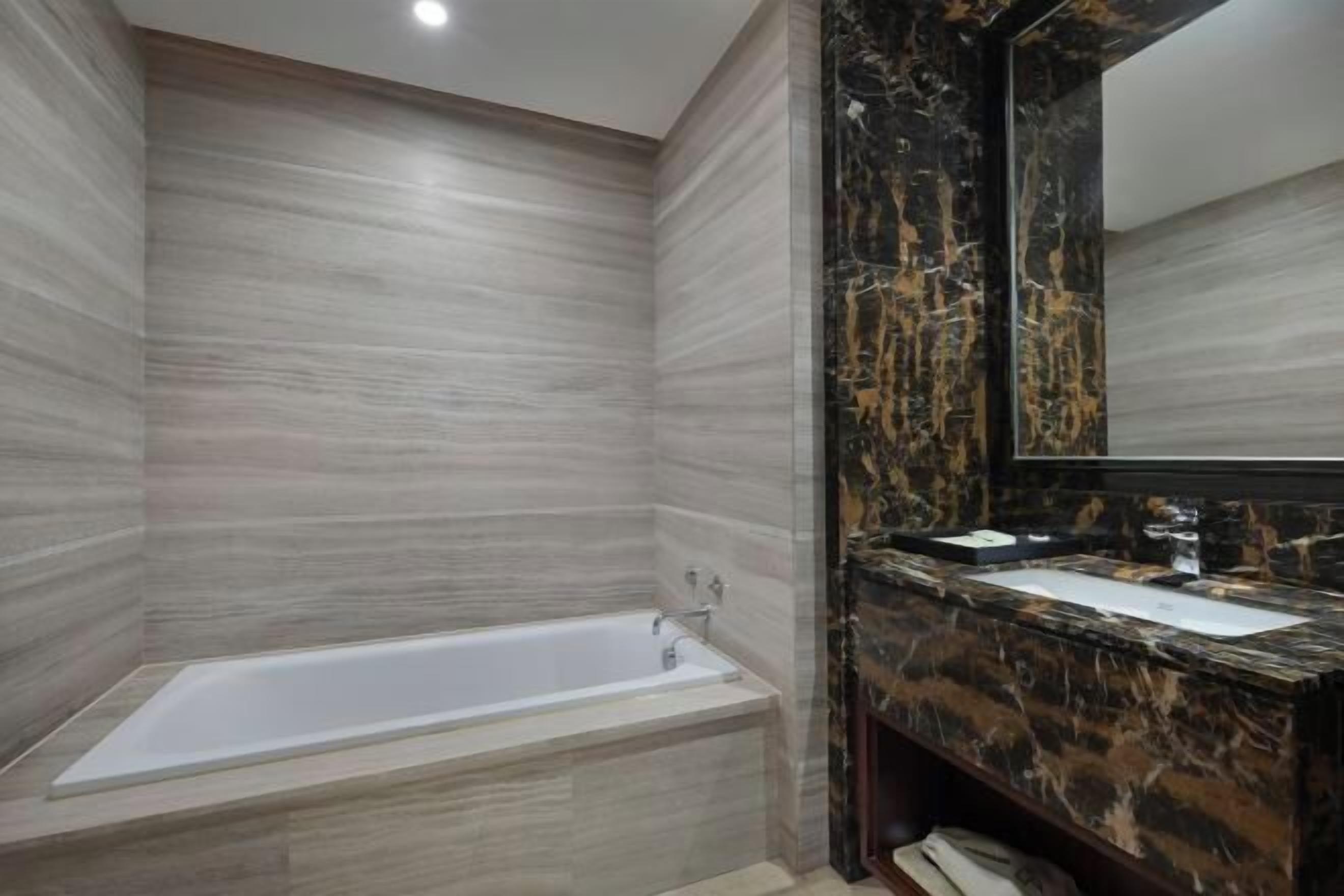 A modern bathroom with a marble vanity, a bathtub, and a large mirror.