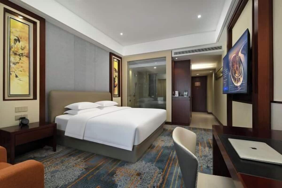 A hotel room with a bed, desk, chair, and a TV.