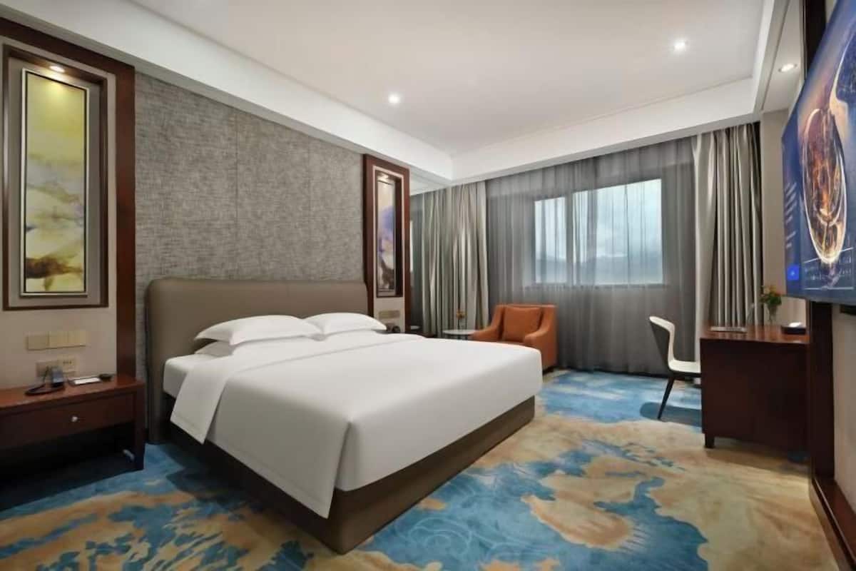 A hotel room with a large bed, a desk, a chair, and a TV.
