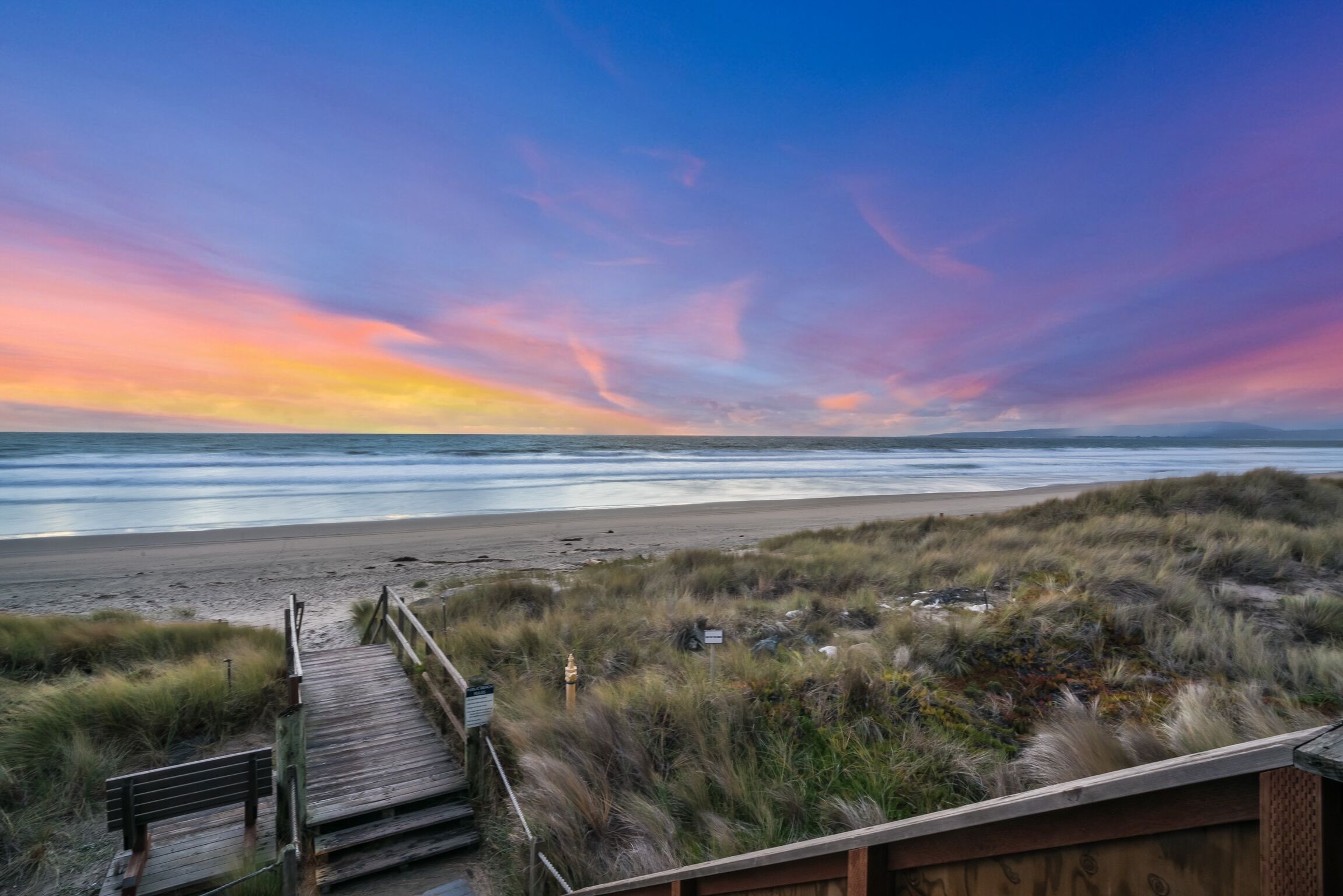 A wooden boardwalk leading to a beach with a sunset in the background.