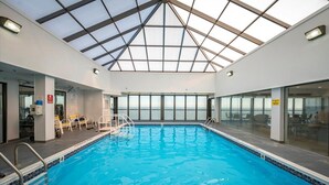 An indoor swimming pool with a glass ceiling, clear view of the sky, and a seating area with chairs.