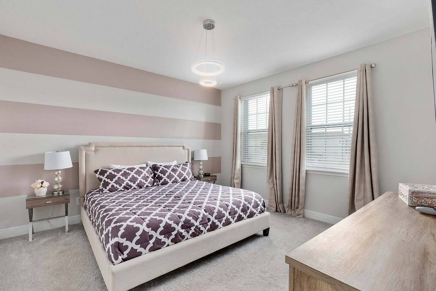A bedroom with a bed, two bedside tables, a nightstand, a desk, and a window with curtains.