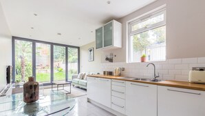 A modern kitchen with white cabinets, a glass-top table, and a window with a view of greenery.