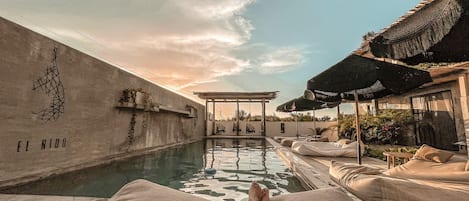 A poolside view with lounge chairs, a pergola, and a wall with 'EL NIDO' text.