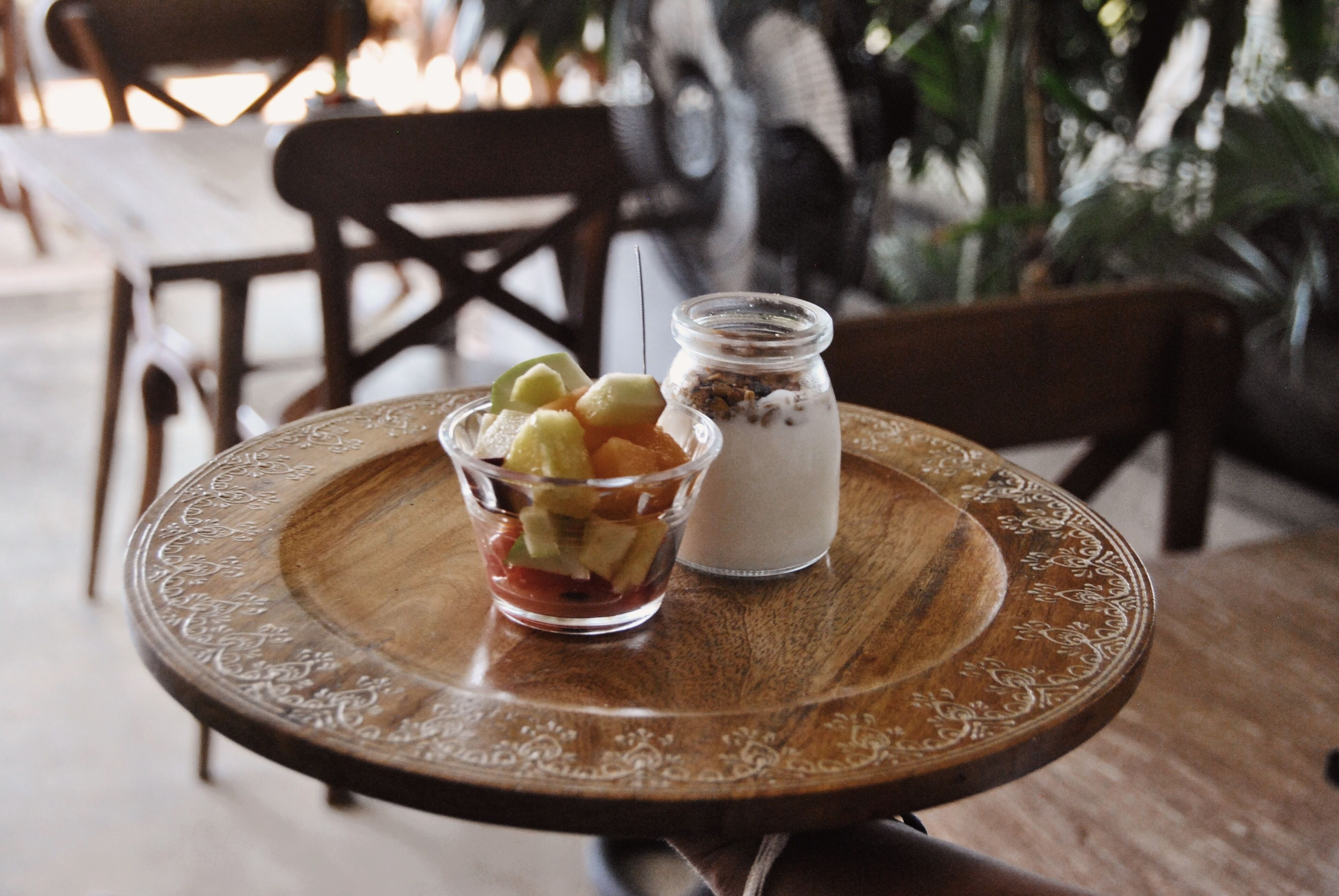A wooden table with a glass bowl containing fruit and a jar of yogurt.