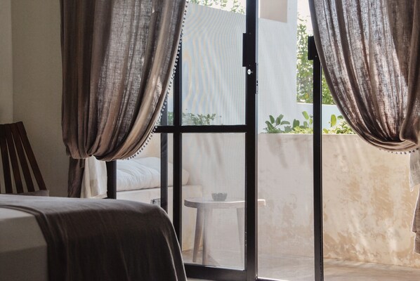 Un dormitorio con cama, cortinas, una ventana y vistas a un balcón con mesa y plantas.
