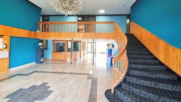 Un hall d’entrée spacieux avec un escalier en bois, un lustre et un comptoir d’accueil.