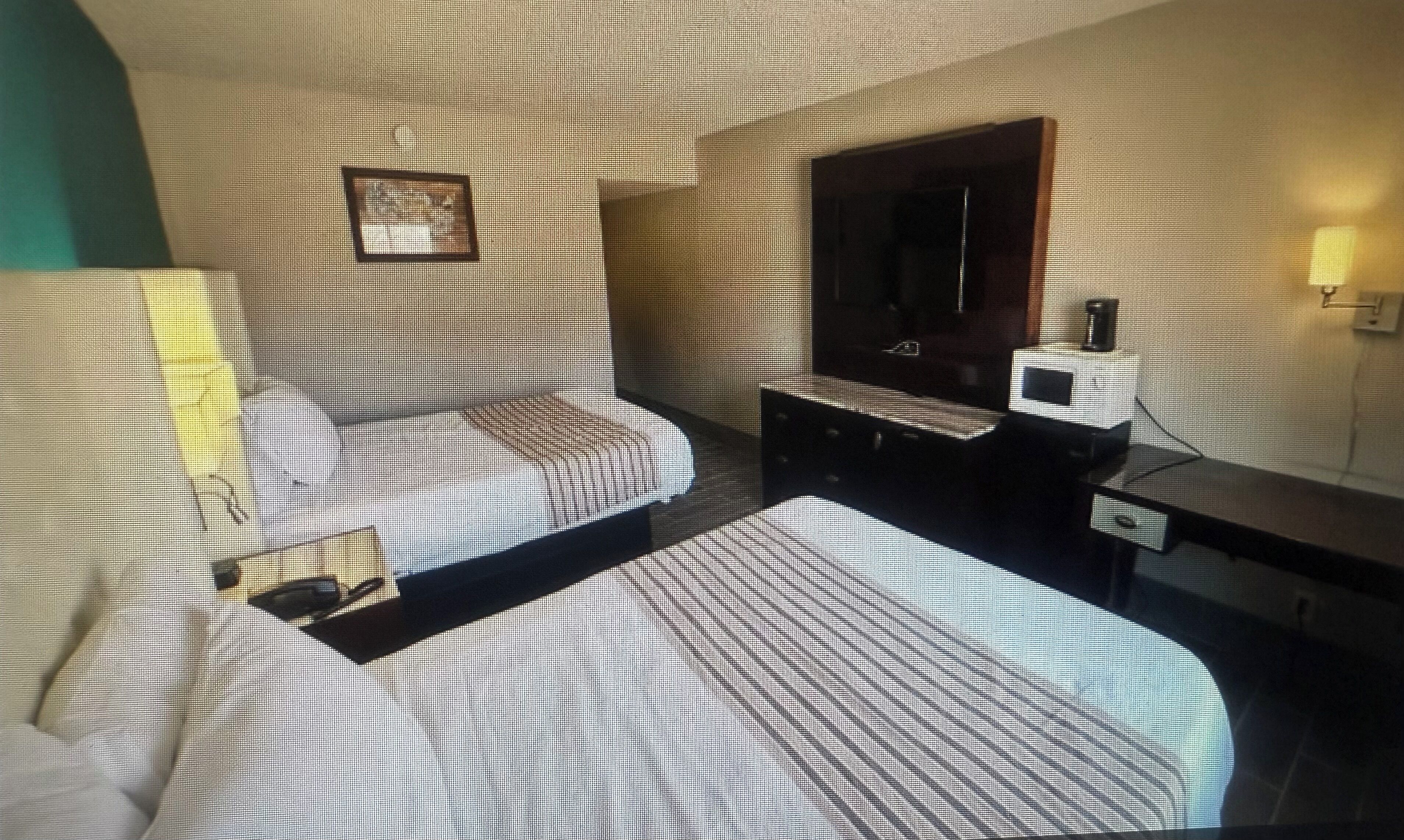 A hotel room with a bed, a bedside table, a mirror, and a small desk with a lamp.