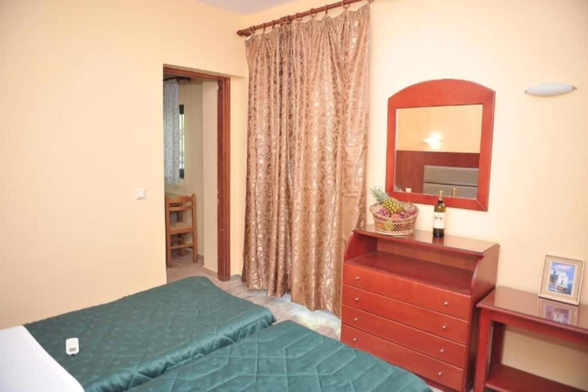 Ein Schlafzimmer mit Bett, Kommode, Spiegel und einem Fenster mit Vorhängen.