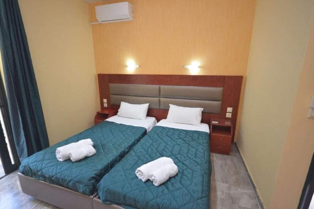 Ein Hotelzimmer mit zwei Betten, jeweils mit einer grünen Decke und weißen Kissen, einem hölzernen Kopfteil, Nachttischlampen und einem kleinen Nachttisch.