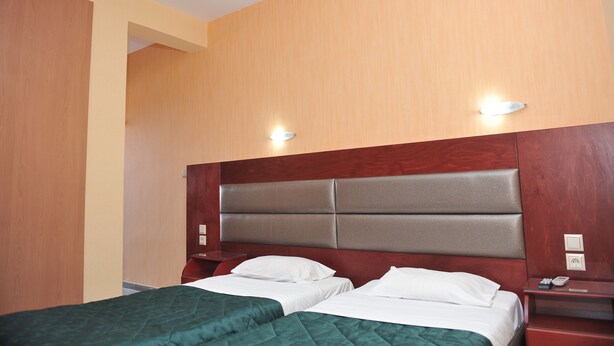 Ein Hotelzimmer mit zwei Betten, Holz-Kopfteilen und Nachttischen mit Lampen.