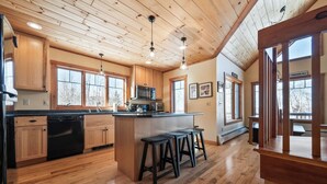 Una cocina amplia con armarios de madera, una isla central con taburetes y ventanas grandes.