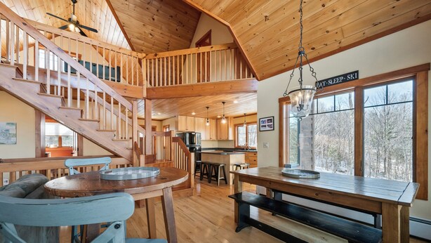 Un interior de madera con una escalera, comedor, cocina y ventanas amplias.