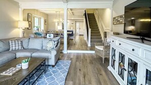 Ein Wohnzimmer mit Sofa, Couchtisch und Fernsehschrank. Eine Treppe führt zu einem anderen Raum.