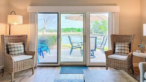 Ein Zimmer mit zwei Korbstühlen, einem kleinen Tisch und einer großen Schiebeglastür, die auf eine Terrasse im Freien führt.