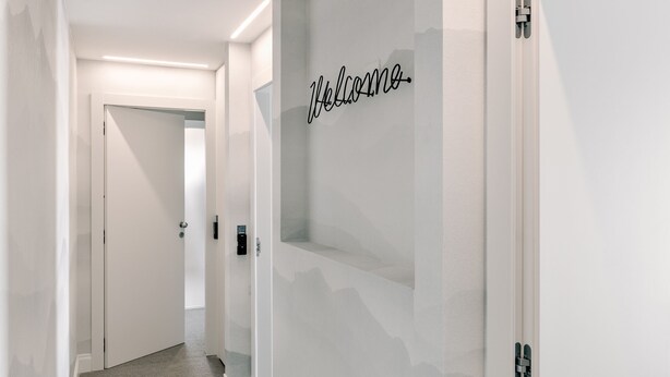 A modern hallway with a carpeted floor, a glass wall with a 'Welcome' sign, and a door at the end. - Anjoy & Bleev Rooms | SARDINA | Queen French bed room (Rho)