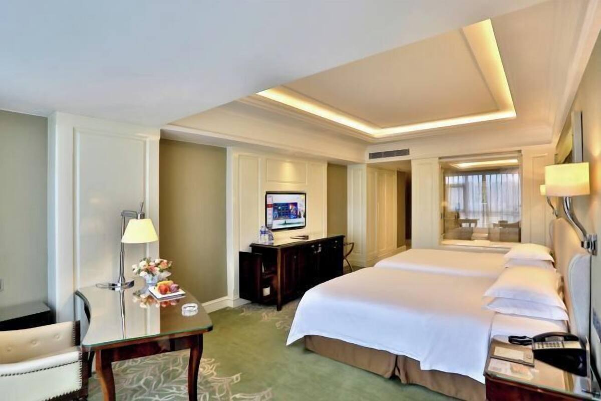 A hotel room with a large bed, a desk with a lamp, a television, and a view of a balcony.