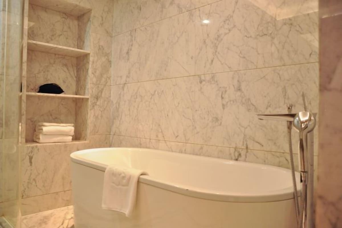 A bathroom with a freestanding bathtub, marble walls, and a shelf with folded towels.