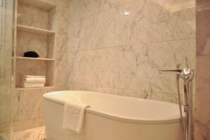 A bathroom with a freestanding bathtub, marble walls, and a shelf with folded towels.