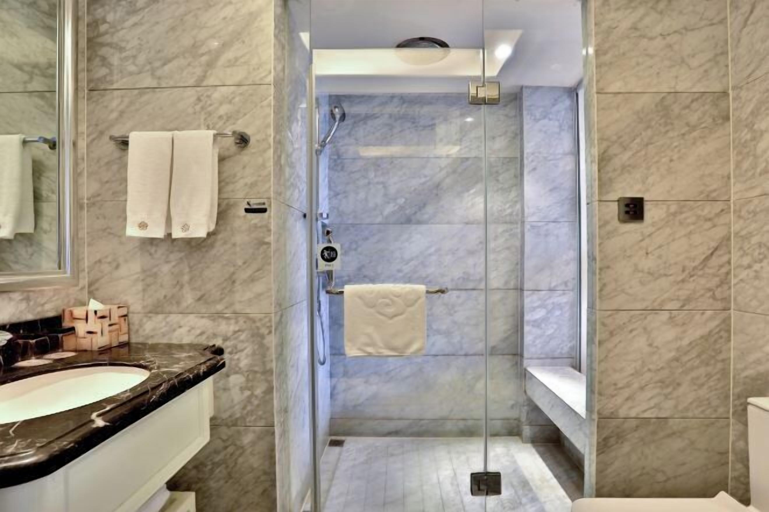A modern bathroom with a glass-enclosed shower, marble walls, and a vanity with a sink and mirror.