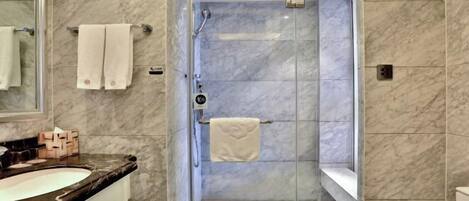 A modern bathroom with a glass-enclosed shower, marble walls, and a vanity with a sink and mirror.