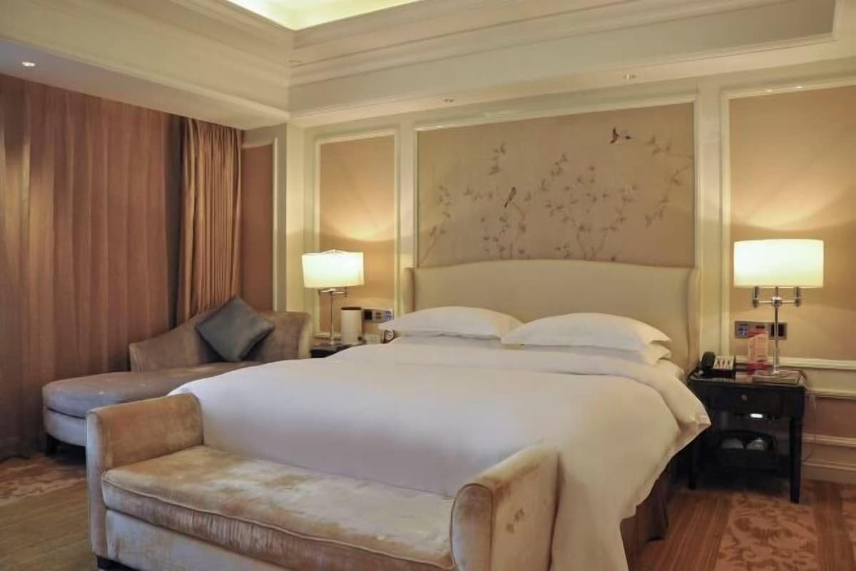 A hotel room with a large bed, two bedside tables, a sofa, and a curtain.