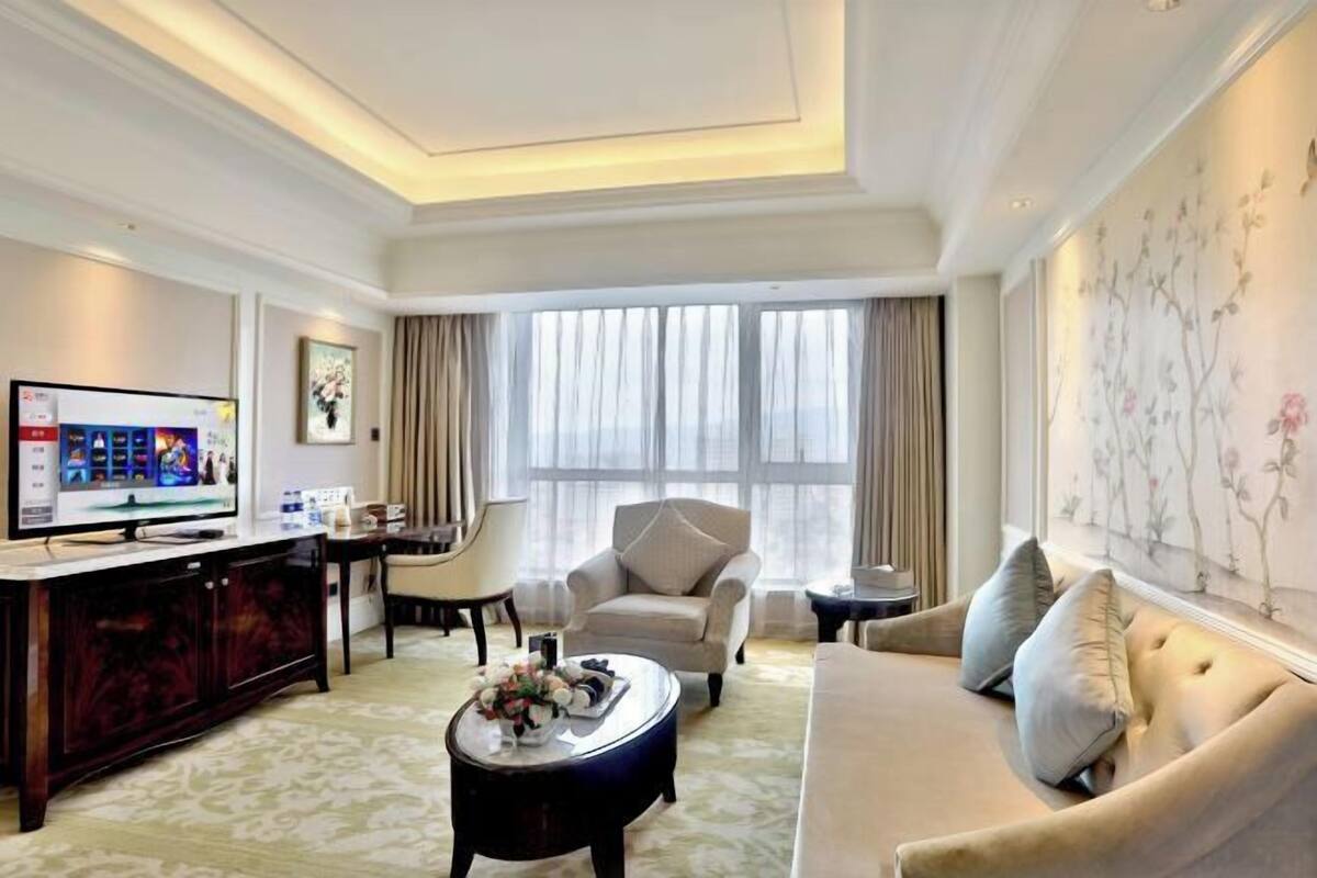 A hotel room with a sofa, armchair, TV, and a decorative wall.
