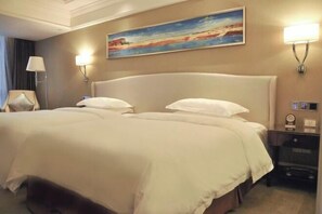 A hotel room with a large bed, two bedside lamps, a painting on the wall, and a nightstand with a clock.