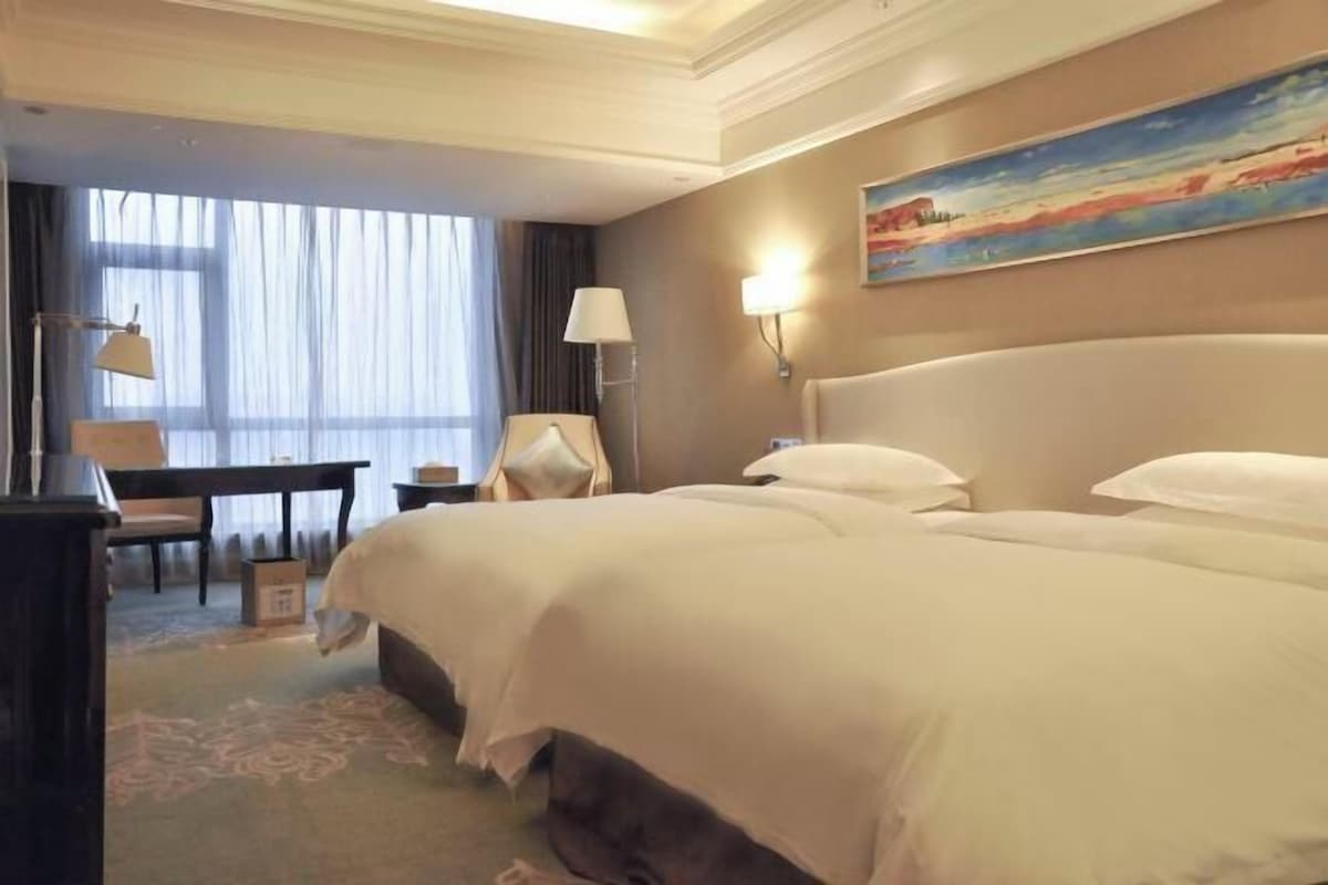 A hotel room with a large bed, a desk, a chair, and a painting on the wall.