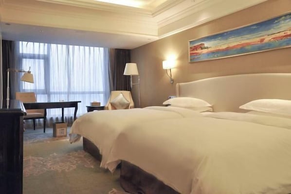 A hotel room with a large bed, a desk, a chair, and a painting on the wall.