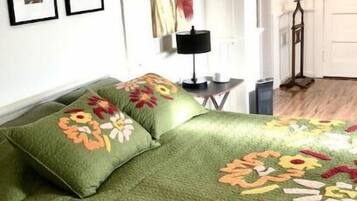 A bedroom with a green bedspread featuring floral patterns, a bedside table with a lamp, and a door leading to another room.