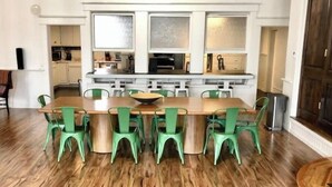 A dining area with a wooden table and green chairs, a kitchen in the background, and a wooden floor. - 4Bd 2Ba Converted Historic Church in Uptown Butte! (Butte)
