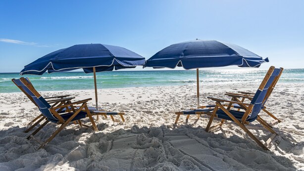 Deux chaises de plage avec des coussins bleus et des parasols assortis, sur une plage de sable.