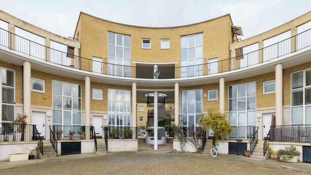 A courtyard with a central staircase, surrounded by brick buildings with balconies and potted plants.