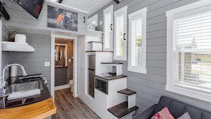 A compact kitchen with a sink, microwave, and built-in oven. There is a gray couch with patterned cushions and a TV mounted on the wall. - Zion Tiny Home • Pet Friendly • Stargazing Deck (Apple Valley)