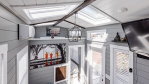 A room with skylights, a bed, a TV, and artwork on the walls. - Zion Tiny Home • Pet Friendly • Stargazing Deck (Apple Valley)