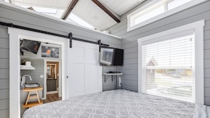 A bedroom with a large bed, a TV mounted on the wall, and a window with blinds. - Zion Tiny Home • Pet Friendly • Stargazing Deck (Apple Valley)