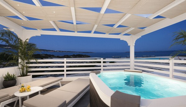 A rooftop pool area with a view of the sea, lounge chairs, and a hot tub.