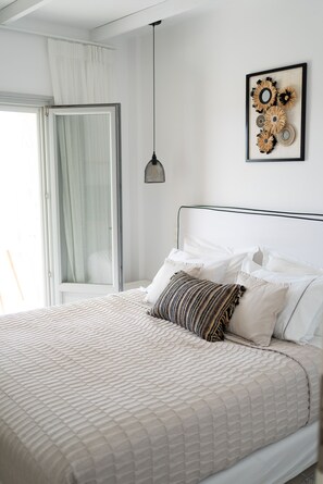 A neatly made bed with a quilted cover, a hanging pendant light, and a framed artwork on the wall.