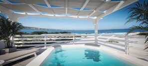 A modern outdoor pool area with a clear view of the sea and distant coastline.