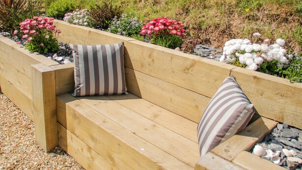 A wooden bench with two striped cushions in a garden setting. - 14 Parc Delfryn (Brynteg)