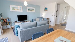A modern living room with a grey sofa, a wooden dining table, and a TV. - 14 Parc Delfryn (Brynteg)
