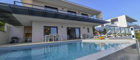 A modern house with a swimming pool, outdoor seating, and a slide.