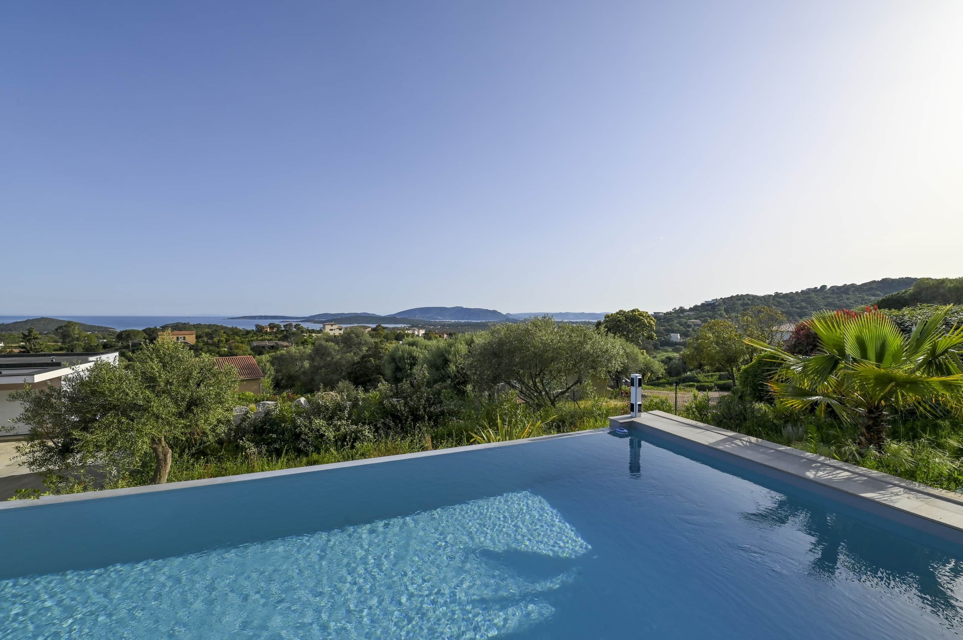 A clear blue infinity pool with a view of the sea and hills.