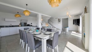 Eine moderne Küche mit weißen Schränken, ein Essbereich mit weißem Tisch und grauen Stühlen sowie eine Treppe, die zu einer weiteren Ebene führt.
