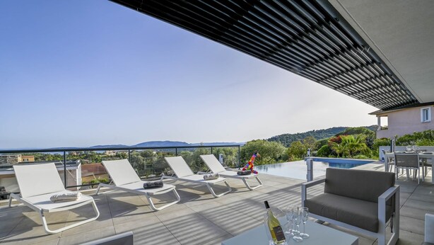 Eine Dachterrasse mit weißen Liegestühlen, einem Tisch mit Flasche und Gläsern sowie einem Pool im Hintergrund.